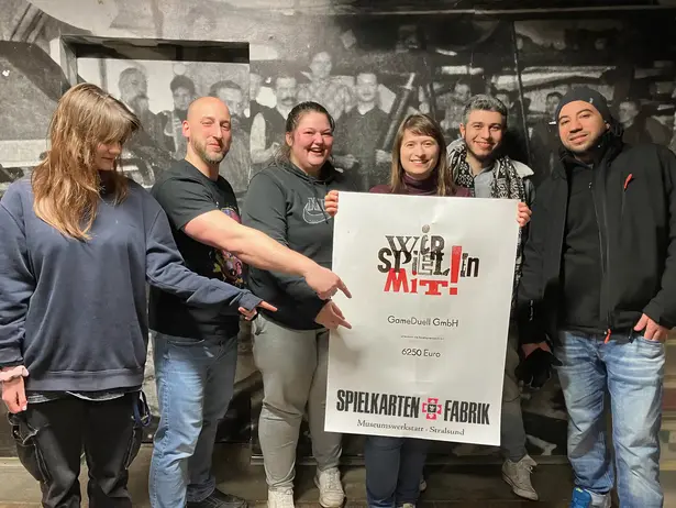 Group photo, the team of the playing card factory points to a donation poster ©SPEICHER_Leute e.V.